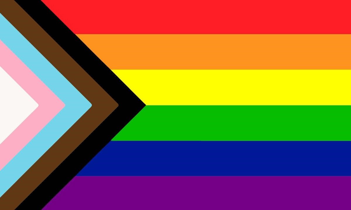 A six color norizontally striped flag: red, orange, yellow, green, blue, purple. On the left side of the flag a striped triangle points to the right in white, pink, pale blue, brown, and black